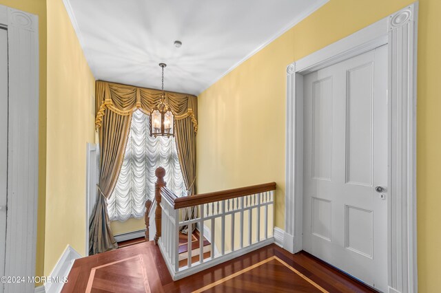 staircase featuring hardwood / wood-style flooring, crown molding, a baseboard radiator, and an inviting chandelier