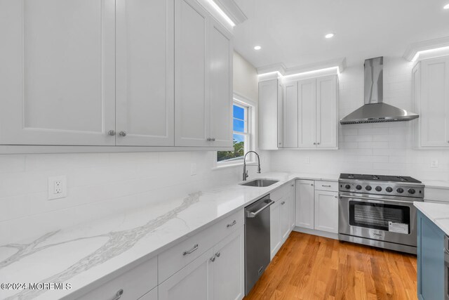 kitchen featuring appliances with stainless steel finishes, wall chimney range hood, sink, backsplash, and light hardwood / wood-style floors