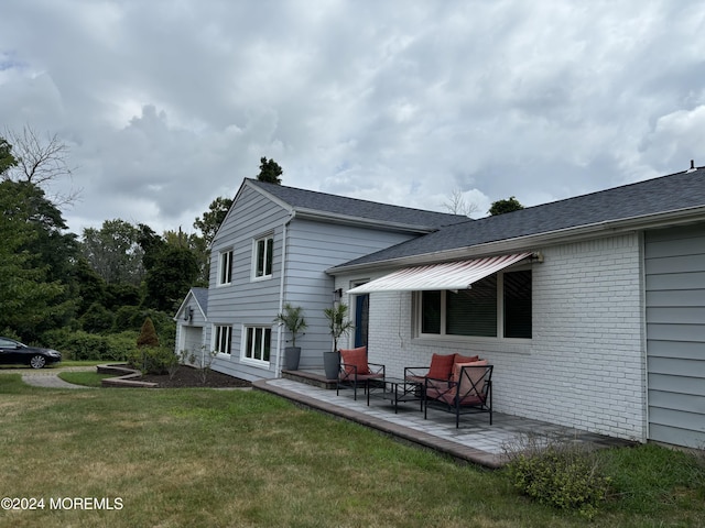 rear view of house featuring brick siding, a lawn, a patio area, and a shingled roof