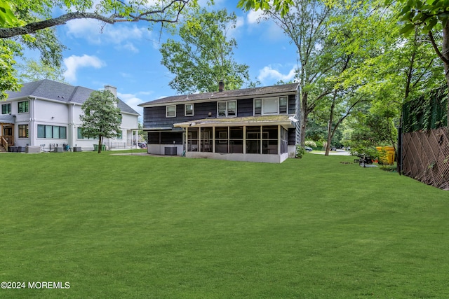 rear view of house featuring a lawn, a chimney, fence, and a sunroom