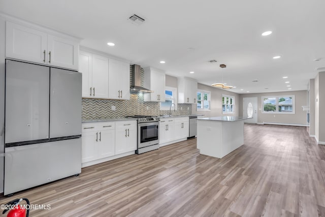 kitchen featuring baseboard heating, appliances with stainless steel finishes, wall chimney range hood, and white cabinets