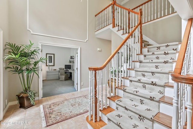 staircase with tile patterned flooring, baseboards, and a high ceiling