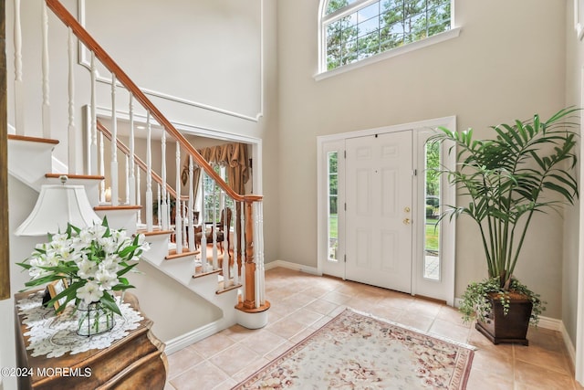 tiled entrance foyer with stairs, a high ceiling, and baseboards