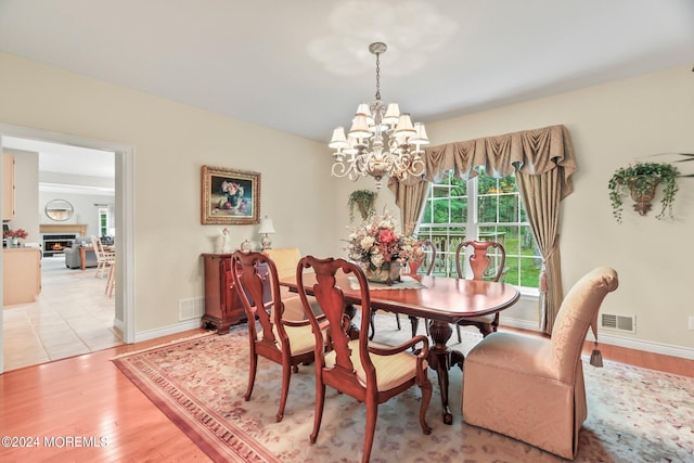 dining space with light wood finished floors, a lit fireplace, visible vents, and an inviting chandelier