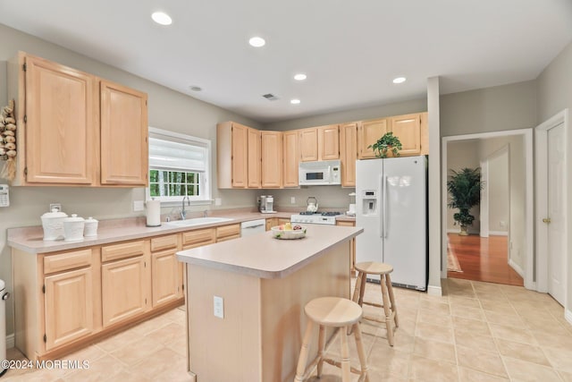 kitchen featuring white appliances, a kitchen breakfast bar, light countertops, light brown cabinetry, and a sink