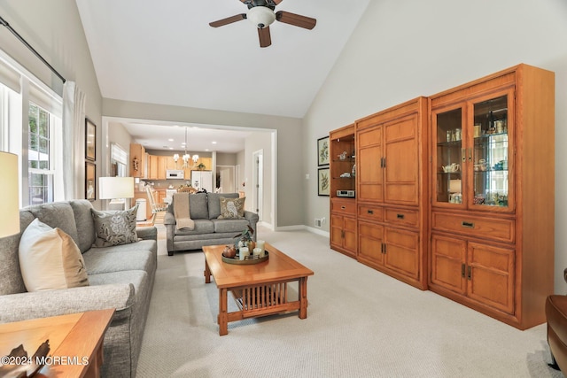 living area featuring ceiling fan with notable chandelier, high vaulted ceiling, baseboards, and light colored carpet