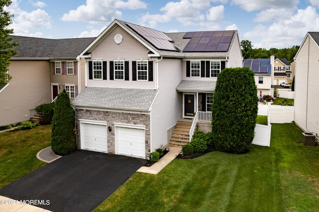 view of front of property featuring solar panels, central AC unit, a garage, and a front lawn