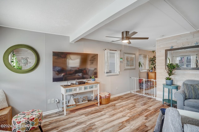 sitting room with baseboards, a ceiling fan, light wood-style flooring, a textured ceiling, and beam ceiling