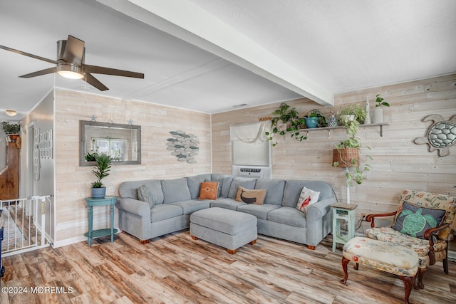 living area featuring beam ceiling, ceiling fan, wooden walls, light wood-type flooring, and baseboards