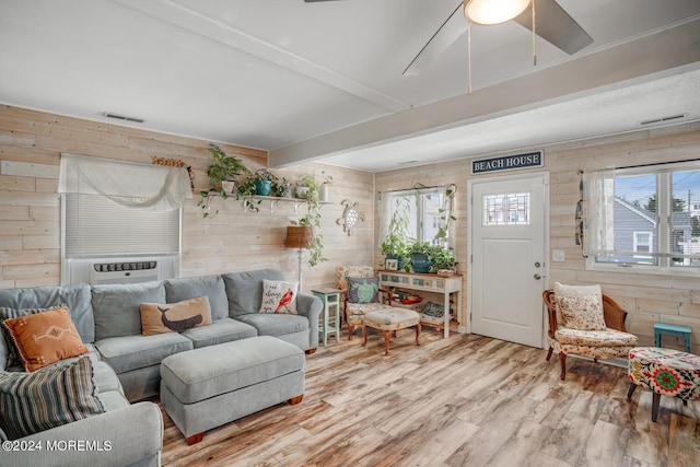 living room with cooling unit, wooden walls, visible vents, light wood-type flooring, and beamed ceiling