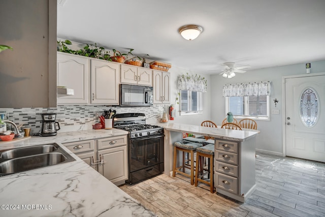 kitchen with light stone counters, a sink, a peninsula, and black appliances