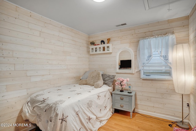 bedroom with light wood finished floors, visible vents, and wood walls