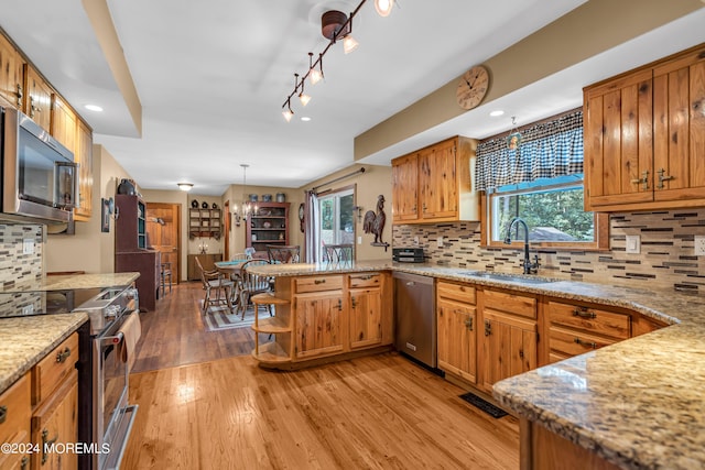 kitchen featuring sink, light hardwood / wood-style flooring, stainless steel appliances, decorative light fixtures, and kitchen peninsula