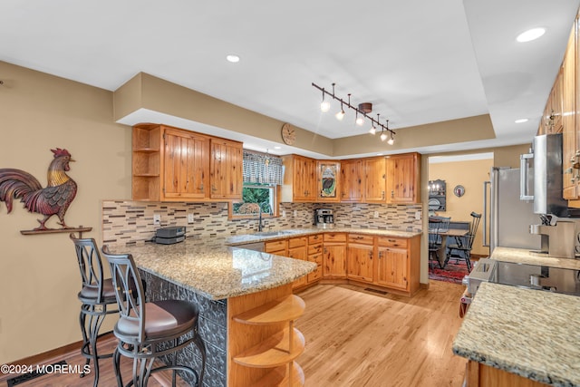 kitchen with sink, a breakfast bar area, backsplash, kitchen peninsula, and light hardwood / wood-style flooring