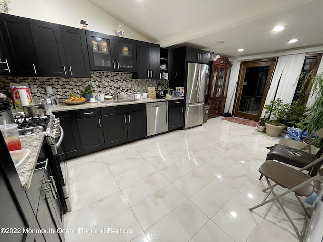 kitchen with lofted ceiling, stainless steel appliances, light stone countertops, sink, and decorative backsplash