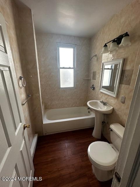 bathroom with tile walls, tiled shower / bath, hardwood / wood-style floors, a baseboard heating unit, and toilet