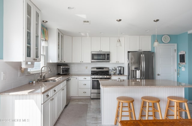 kitchen featuring sink, decorative light fixtures, appliances with stainless steel finishes, light hardwood / wood-style floors, and white cabinets