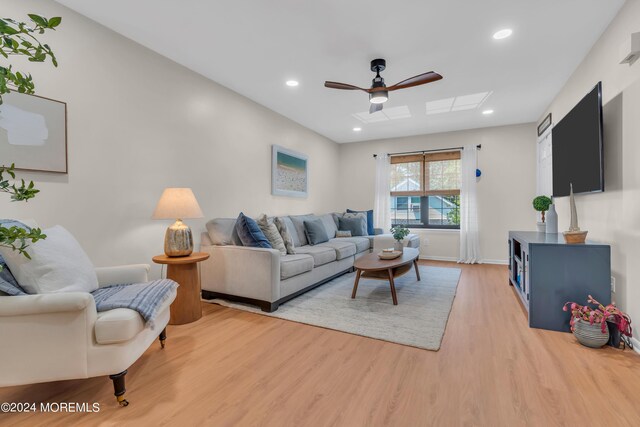 living room with a skylight, light hardwood / wood-style floors, and ceiling fan