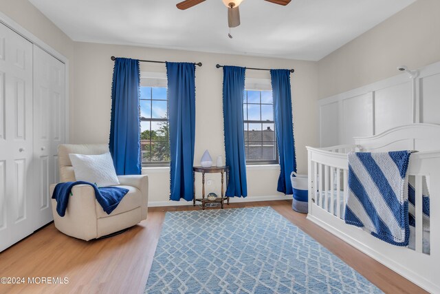 bedroom with a crib, a closet, wood-type flooring, and ceiling fan