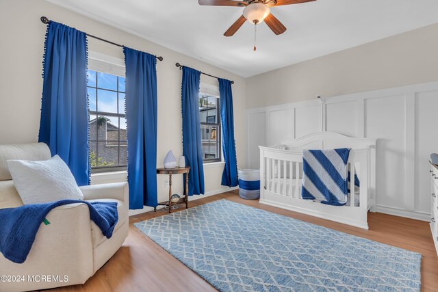 bedroom with ceiling fan, light wood-type flooring, and a nursery area