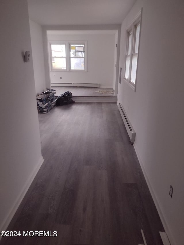 corridor with baseboards, a baseboard heating unit, and dark wood-type flooring