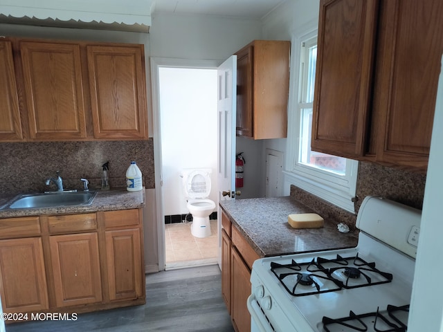 kitchen with brown cabinetry, a sink, and white range with gas stovetop