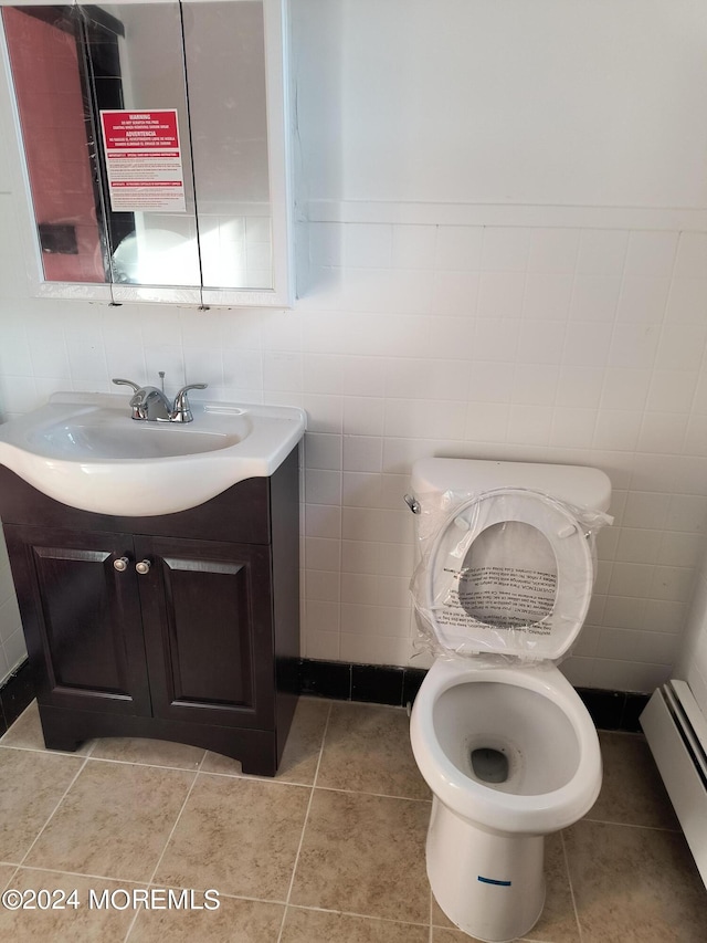 bathroom featuring toilet, a baseboard radiator, tile patterned flooring, vanity, and tile walls