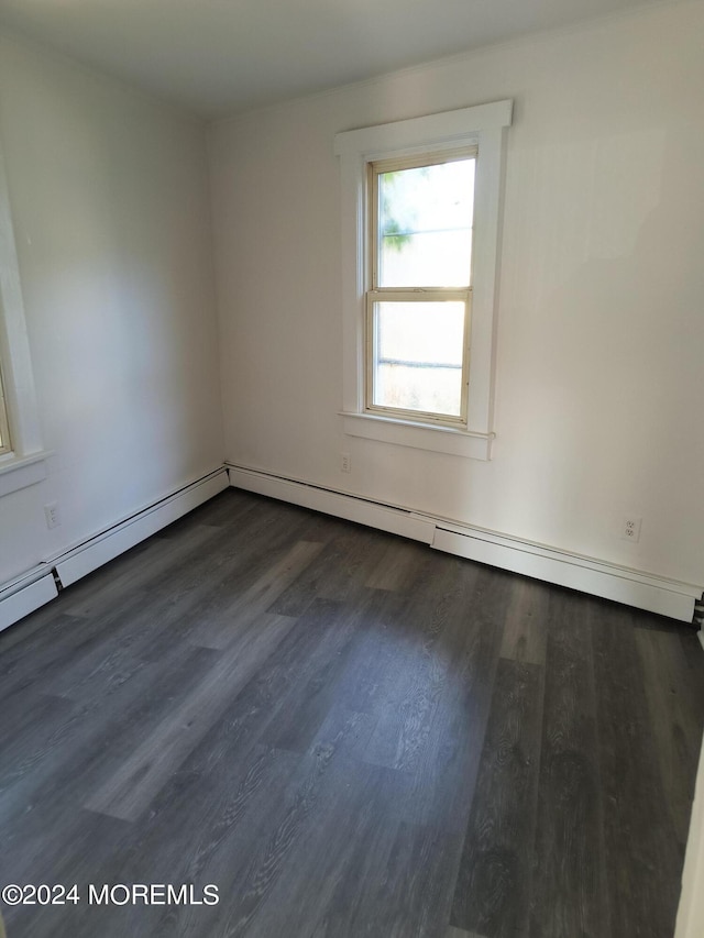 spare room featuring a baseboard heating unit and dark wood-type flooring