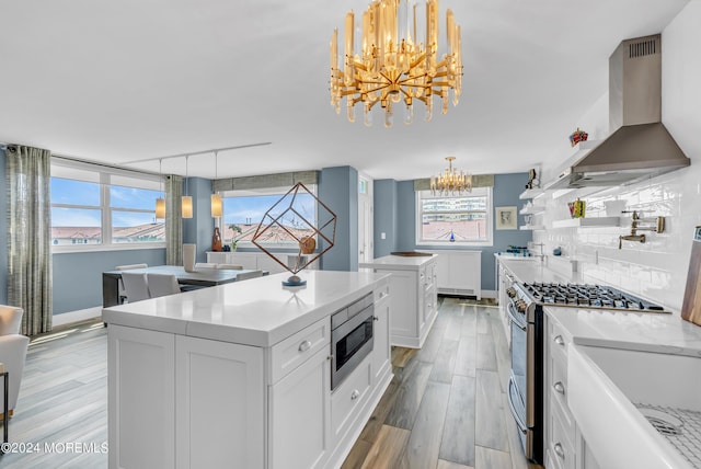 kitchen with stainless steel appliances, wall chimney range hood, pendant lighting, a kitchen island, and white cabinetry