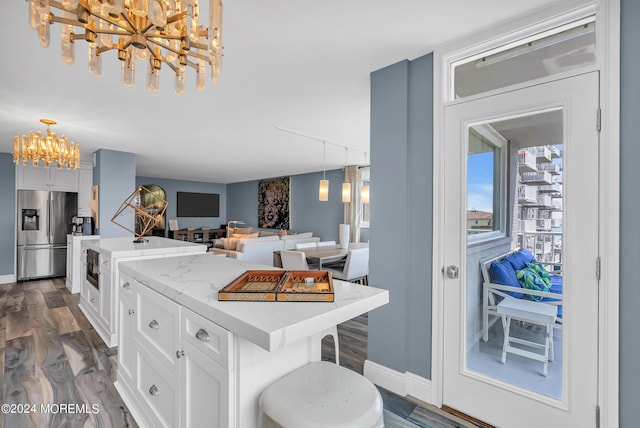 kitchen with a breakfast bar area, stainless steel refrigerator with ice dispenser, decorative light fixtures, a kitchen island, and white cabinetry