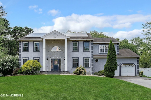 greek revival inspired property featuring a front lawn, roof mounted solar panels, driveway, and an attached garage