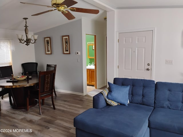 living area featuring ceiling fan with notable chandelier, wood finished floors, baseboards, vaulted ceiling, and ornamental molding