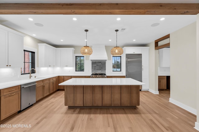 kitchen featuring premium range hood, appliances with stainless steel finishes, decorative light fixtures, a kitchen island, and sink