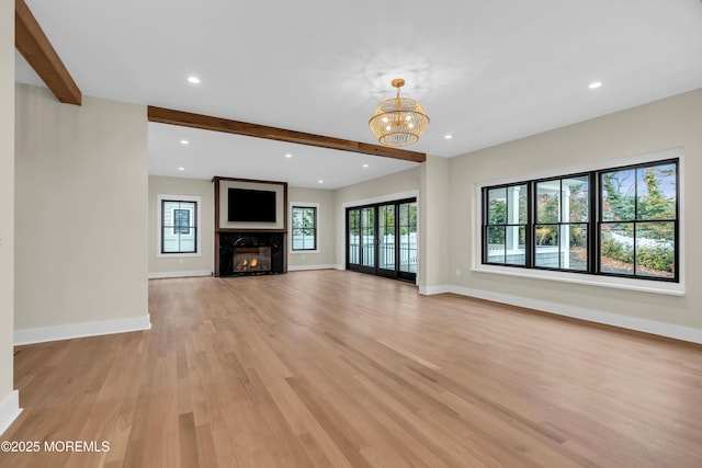 unfurnished living room with light wood-type flooring, a fireplace, french doors, a chandelier, and beam ceiling