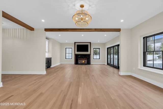 unfurnished living room with light hardwood / wood-style flooring, a high end fireplace, beamed ceiling, and an inviting chandelier