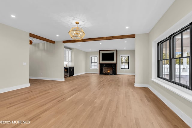 unfurnished living room with wine cooler, light hardwood / wood-style floors, a premium fireplace, an inviting chandelier, and beamed ceiling