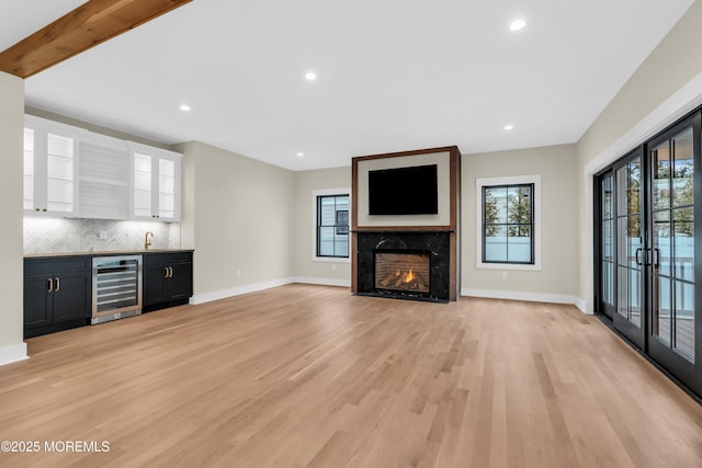 unfurnished living room featuring light hardwood / wood-style floors, a premium fireplace, indoor wet bar, french doors, and beverage cooler