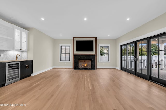 unfurnished living room with light hardwood / wood-style floors, sink, a fireplace, and wine cooler