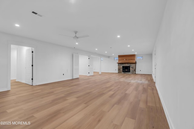 unfurnished living room featuring ceiling fan, a stone fireplace, and light hardwood / wood-style floors