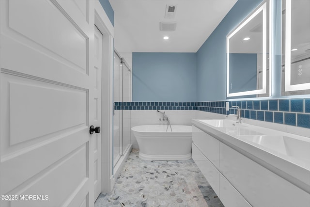 bathroom with independent shower and bath, tile walls, and vanity