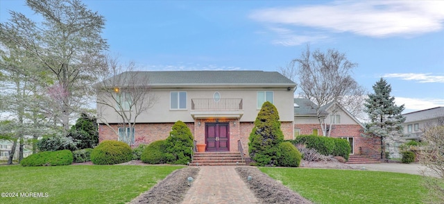 view of front of property featuring brick siding, a front yard, a balcony, and stucco siding