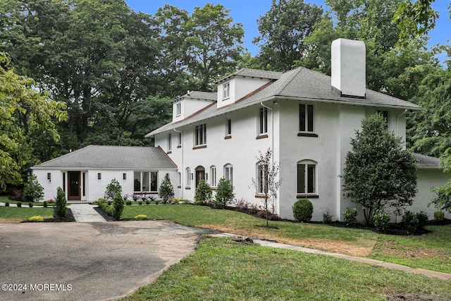 view of front of home with a front lawn, a chimney, a shingled roof, and stucco siding