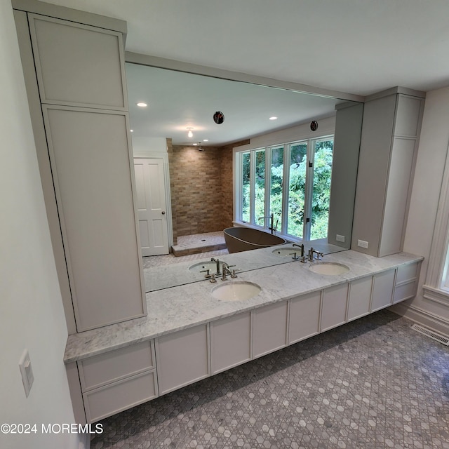 bathroom featuring double vanity, visible vents, a soaking tub, and a sink