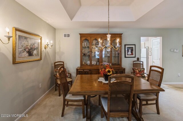 dining space with a raised ceiling, carpet flooring, and a chandelier