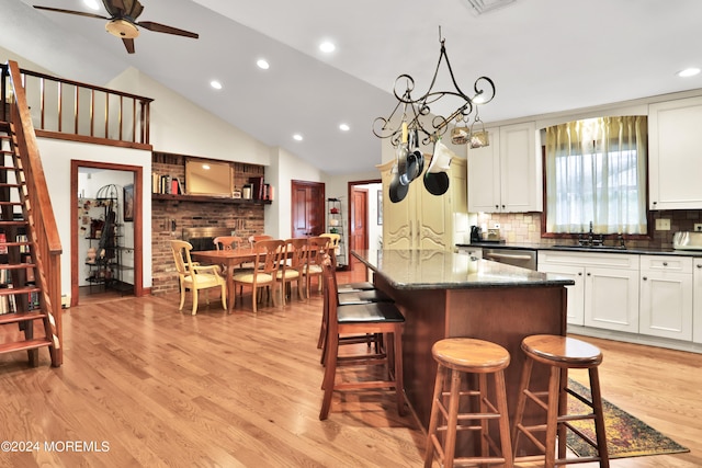 kitchen with decorative backsplash, a breakfast bar area, light wood-type flooring, a fireplace, and ceiling fan with notable chandelier