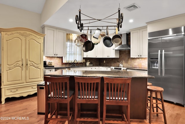 kitchen featuring wall chimney range hood, light wood-type flooring, stainless steel appliances, a notable chandelier, and a center island