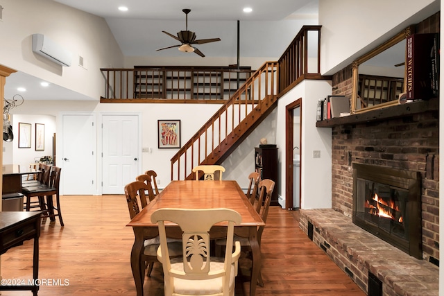 dining area featuring ceiling fan, high vaulted ceiling, wood-type flooring, and a brick fireplace