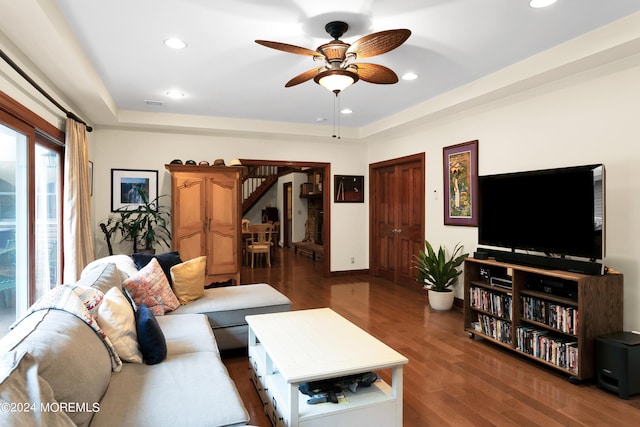 living room with dark wood-type flooring, a raised ceiling, and ceiling fan