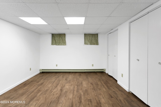 basement with dark wood-type flooring, a drop ceiling, and baseboard heating