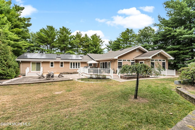 back of house with a wooden deck, a yard, solar panels, and a patio